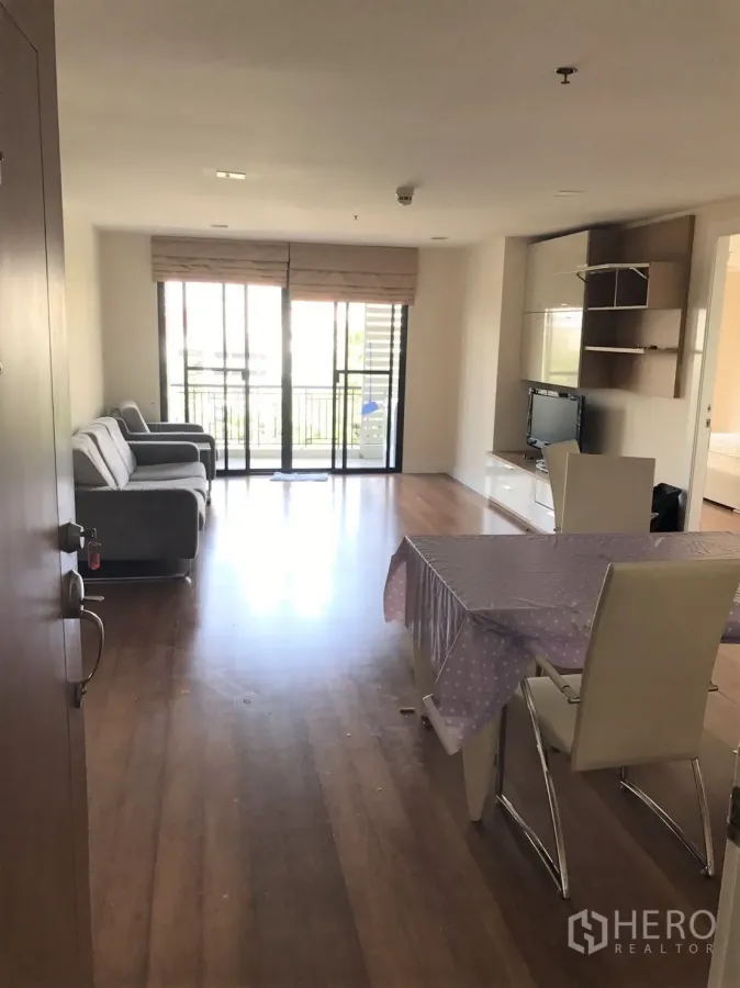 Condominium for rent or sale in Watthana, Bangkok - Bright living and dining area with hardwood floors, TV wall and sliding doors to a balcony.