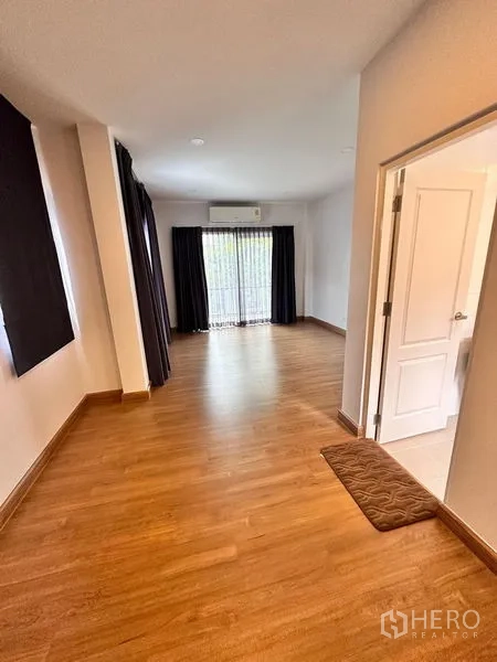Detached House for sale in Prawet, Bangkok - Upstairs hallway with wood floors leading to a bedroom and bathroom, balcony door ahead.