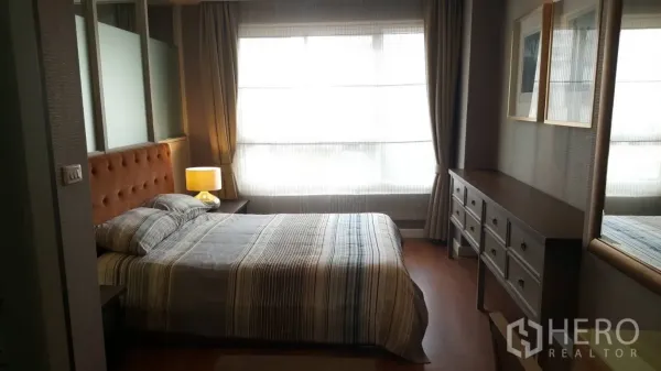 Condominium for rent in Khlong Toei, Bangkok - Cozy bedroom with tufted headboard, bedside lamp, wide window and long dresser.