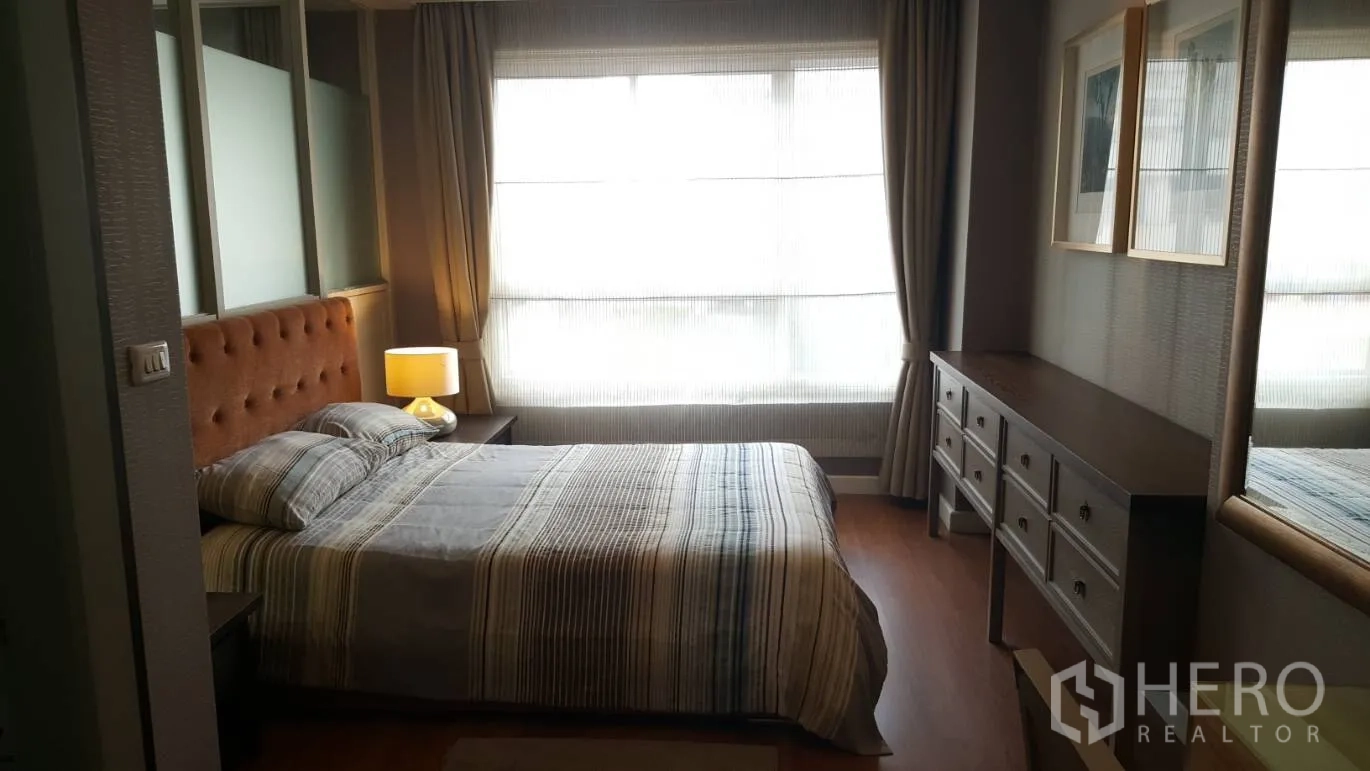Condominium for rent in Khlong Toei, Bangkok - Cozy bedroom with tufted headboard, bedside lamp, wide window and long dresser.