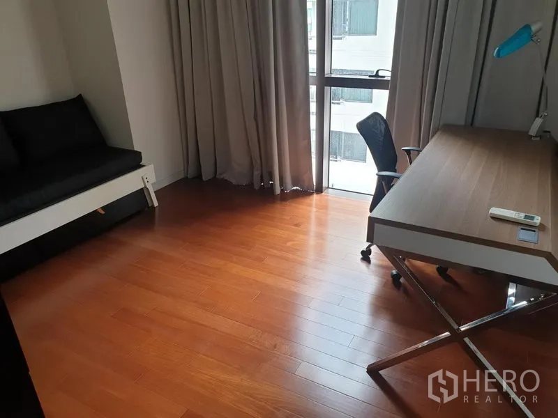 Condominium for rent in Pathum Wan, Bangkok - Flexible room set as a home office with large desk, task chair, wooden floors and full-height window with curtains.