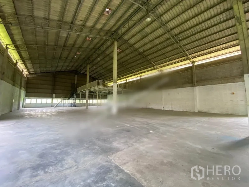 Warehouse for rent in Khlong Sam Wa, Bangkok - Spacious warehouse interior with high steel truss roof, polished concrete floor, and a mezzanine platform with staircase.