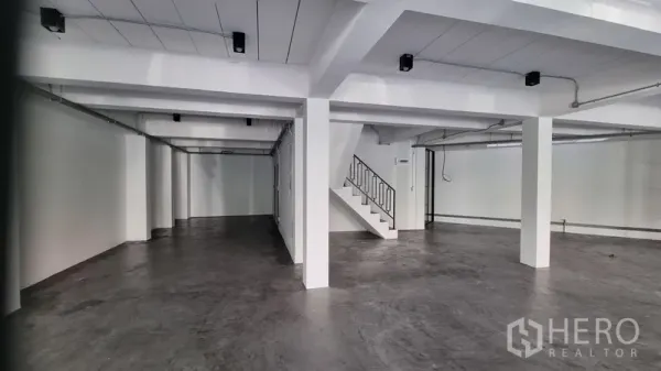 Shophouse for rent in Khlong Toei, Bangkok - Open-plan ground floor with polished concrete flooring, white columns, and exposed ceiling conduits.