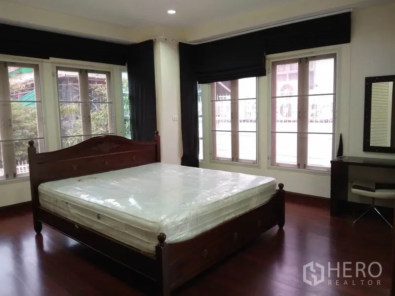 Detached House for rent in Watthana, Bangkok - Master bedroom with king bed, multiple windows, desk and warm wood floors.
