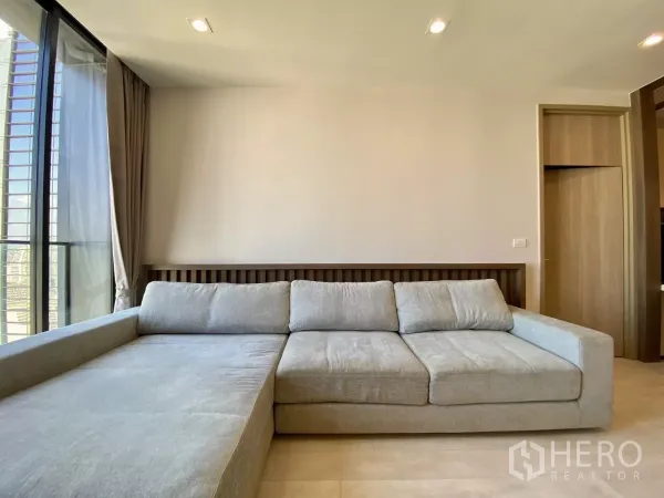Condominium for sale in Pathum Wan, Bangkok - Spacious living room with large L-shaped sofa, full-height glass, and neutral tones.