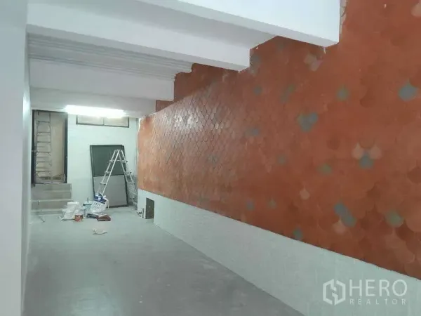 Retail Space for rent in Watthana, Bangkok - Open-plan shop interior with terracotta fish-scale accent wall, white ceiling beams and materials near rear steps.