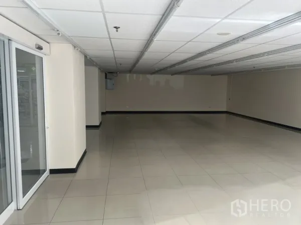 Retail Space for rent in Watthana, Bangkok - Sliding glass entry opens to a large rectangular retail floor with track lighting and neutral walls.
