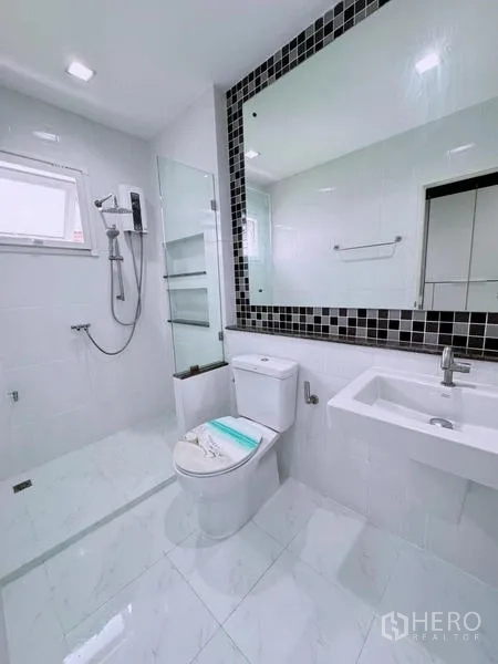 Detached House for rent in Prawet, Bangkok - Bright bathroom with glass shower screen, white tiles, and large mirror.