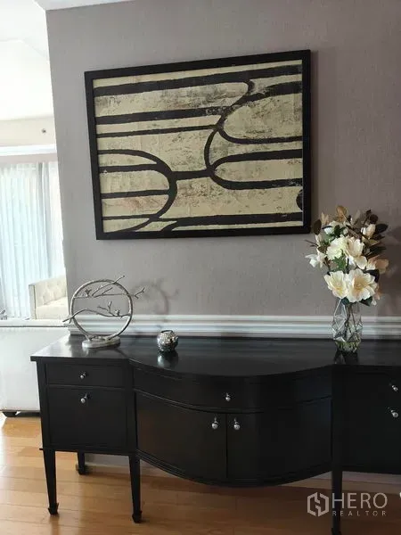 Condominium for rent or sale in Pathum Wan, Bangkok - Elegant console table with decor pieces beneath abstract wall art in a neutral-toned hallway.