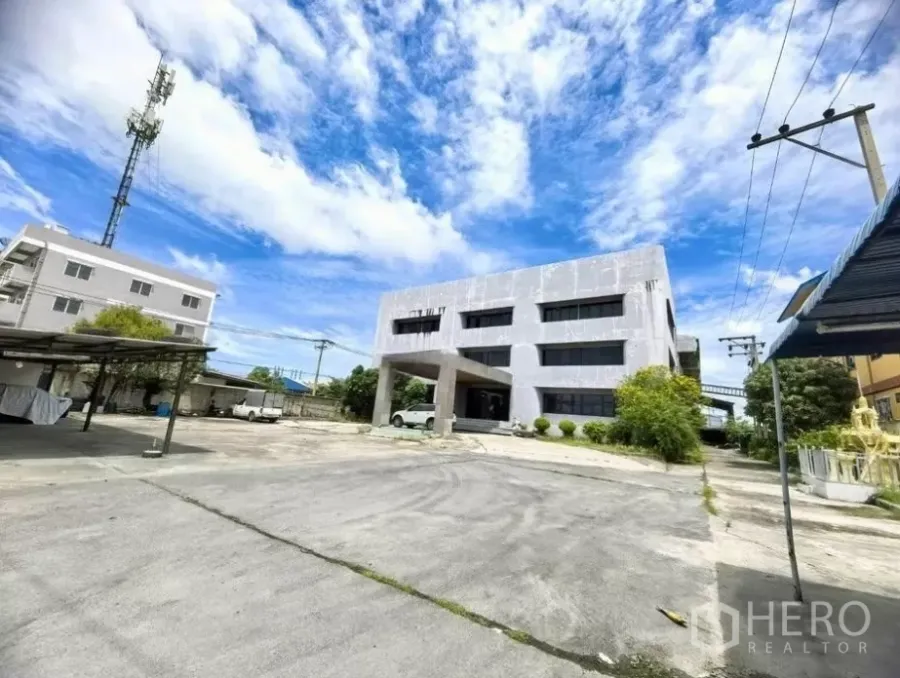 Factory for sale in Bang Phli, Samut Prakan - Wide view of a standalone three-storey office and factory with a large concrete yard and parking.