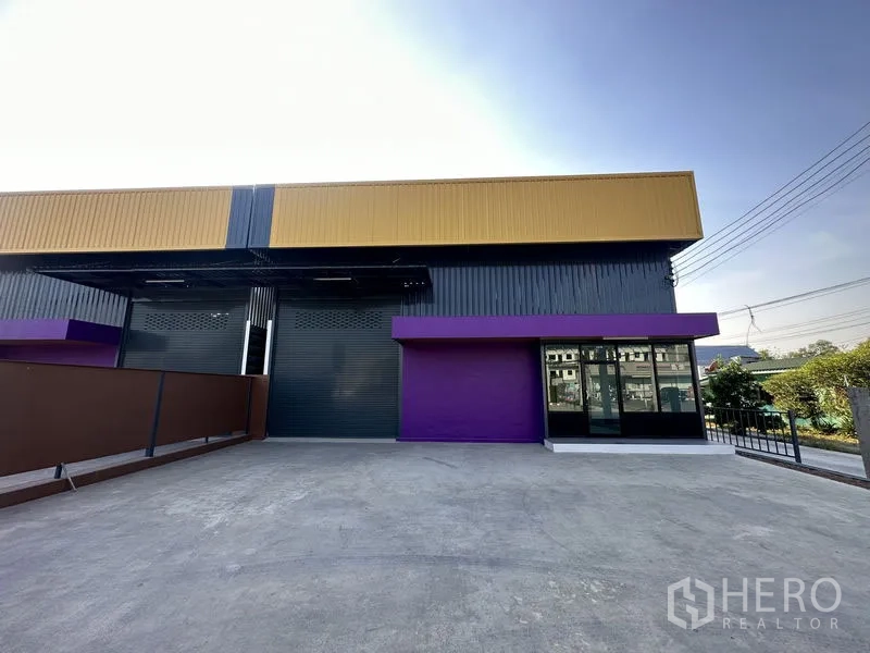 Warehouse for rent in Lam Luk Ka, Pathum Thani - Driveway and loading yard facing the warehouse with a glass-front office on the right.