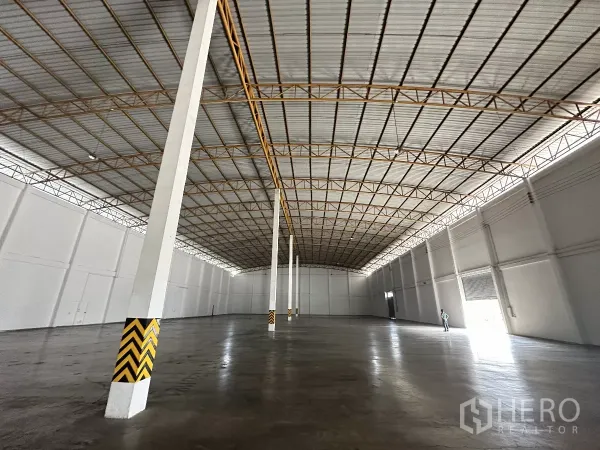 Warehouse for rent in Phra Nakhon Si Ayutthaya - High-ceiling warehouse hall with safety-marked columns, side roller doors, and natural side lighting.