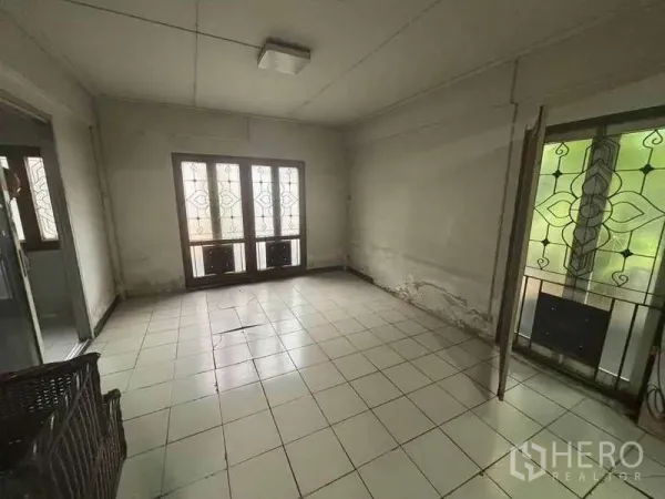 独立式住宅 出租在Suan Luang, Bangkok - 空置的瓷砖房间，大窗与花纹铁艺窗格，墙面有旧痕，具备翻新潜力。