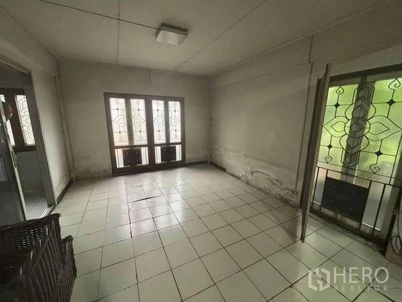 独立式住宅 出租在Suan Luang, Bangkok - 空置的瓷砖房间，大窗与花纹铁艺窗格，墙面有旧痕，具备翻新潜力。