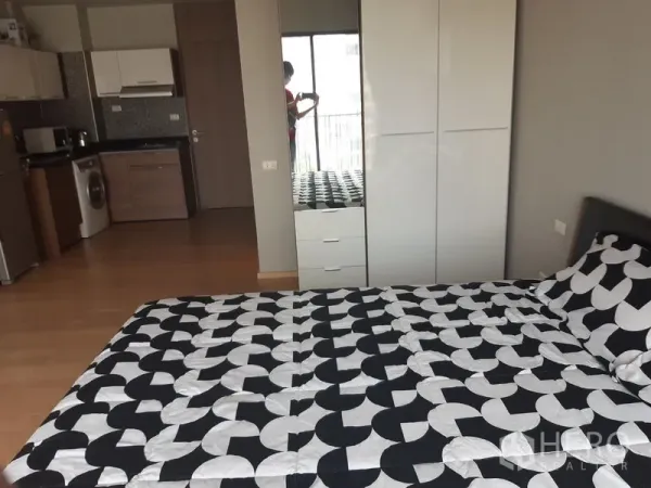 Condominium for rent in Bangkok - Sleeping area with wardrobe and kitchenette in an open-plan condo with wood floors.