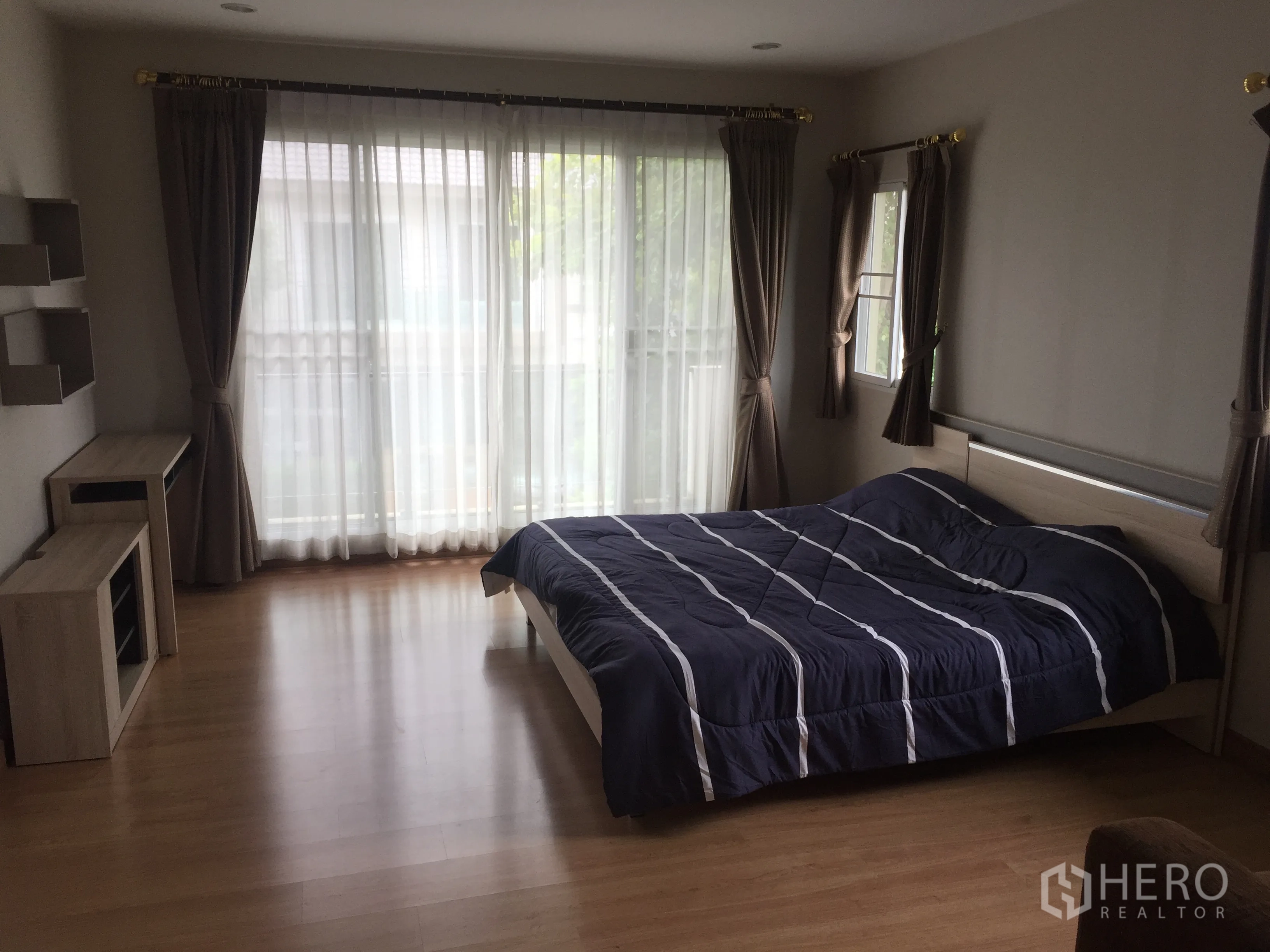 Detached House for rent in Pathum Thani - Spacious master bedroom with wood flooring, large sliding doors to a balcony and a double bed.
