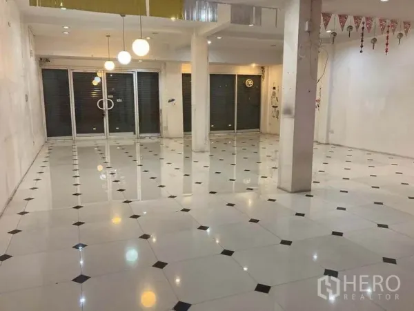 Shophouse for rent in Suan Luang, Bangkok - Spacious ground-floor retail area featuring sliding glass doors, columns, patterned tiles and ceiling lights.