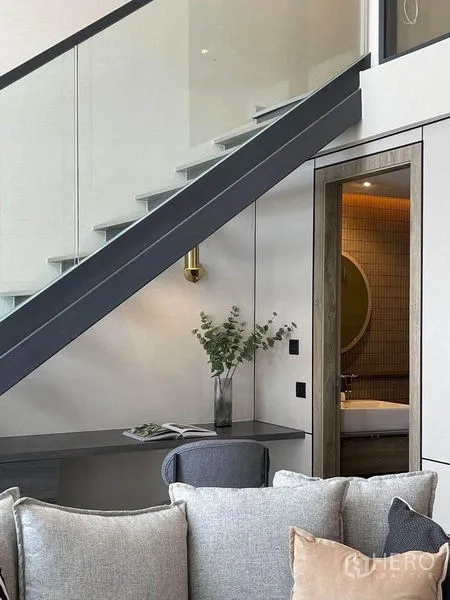 Condominium for rent in Pathum Wan, Bangkok - Open-riser stair above a built-in desk with a doorway to a tiled bathroom featuring a round mirror and warm lighting.