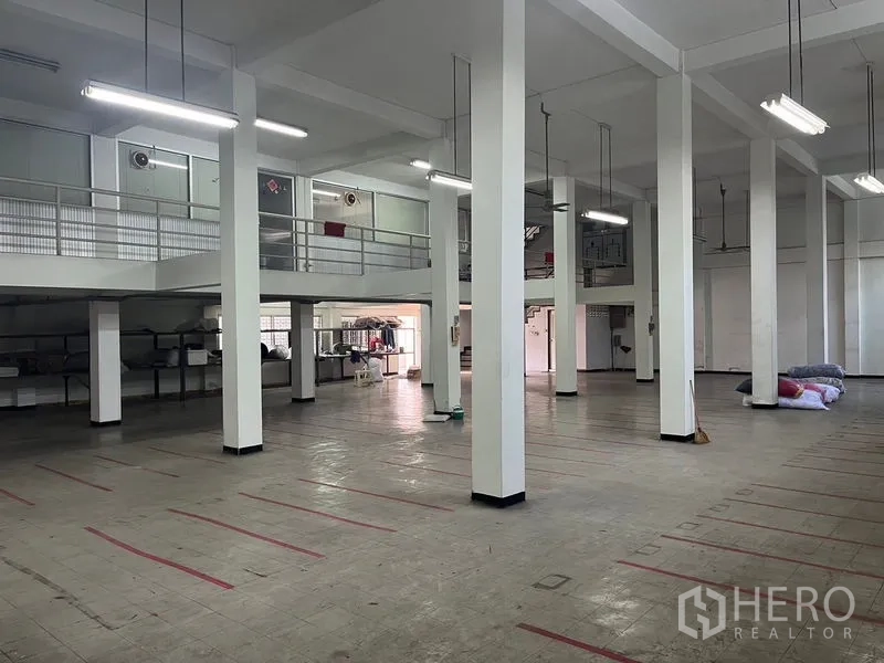 Shophouse for rent in Khlong Toei, Bangkok - Warehouse-style interior featuring tall white columns, mezzanine walkway and bright overhead lighting.