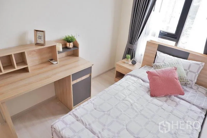 Condominium for rent in Huai Khwang, Bangkok - Second bedroom featuring a work desk, shelving, and bedside table by the window.