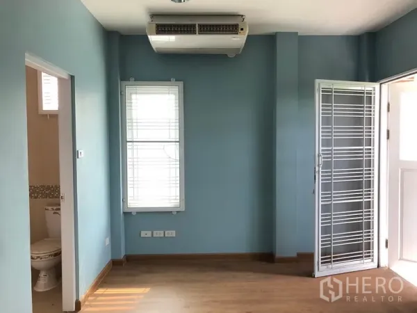 Detached House for sale in Bang Khen, Bangkok - Bright room with blue walls, window blinds, wood flooring, air conditioner and door to an ensuite bathroom.