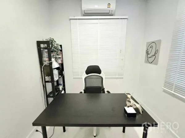 Detached House for rent in Samut Prakan - Minimal home office with black desk, ergonomic chair, shelving and air conditioning.