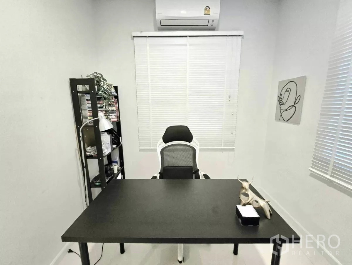 Detached House for rent in Samut Prakan - Minimal home office with black desk, ergonomic chair, shelving and air conditioning.