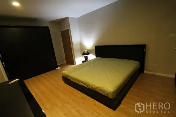 Condominium for rent in Pathum Wan, Bangkok - Second bedroom with dark bed frame, bedside lamp and wood floors.