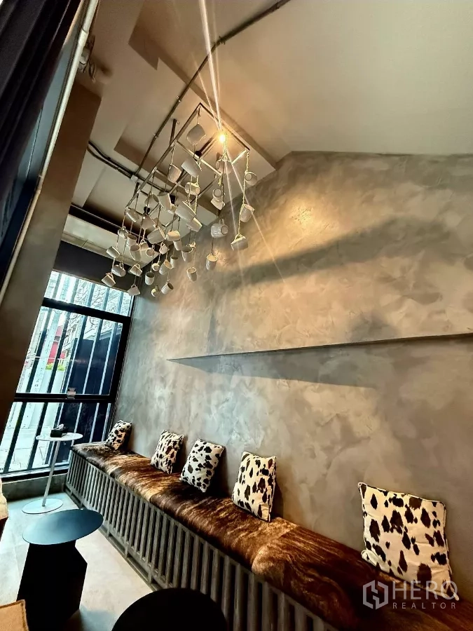 Retail Space for rent in Khlong Toei, Bangkok - Cozy bench seating with cow-print cushions beneath a hanging cup light feature by a floor-to-ceiling window.