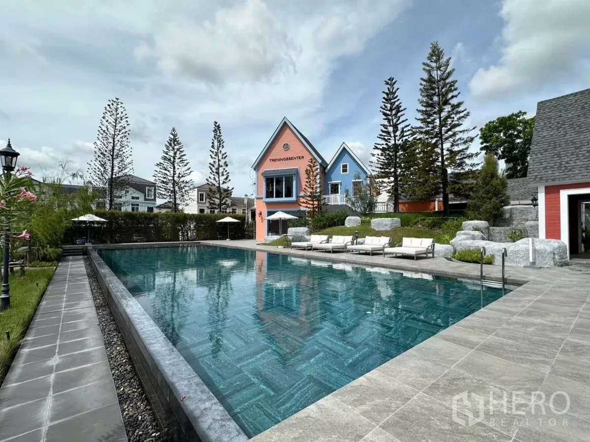Townhouse for rent in Prawet, Bangkok - Outdoor swimming pool with sun loungers and pastel clubhouse buildings.