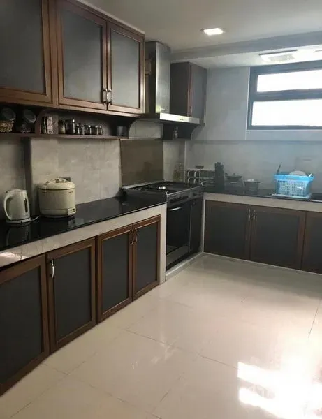 Townhouse for rent in Khlong Toei, Bangkok - Enclosed modern kitchen with dark wood cabinets, black countertops, gas stove, range hood, and a window.