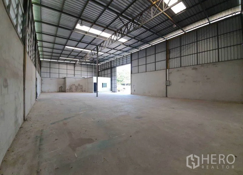 Warehouse for rent in Pathum Thani - Spacious open bay with skylights, a central column, and a large roller door for truck access.