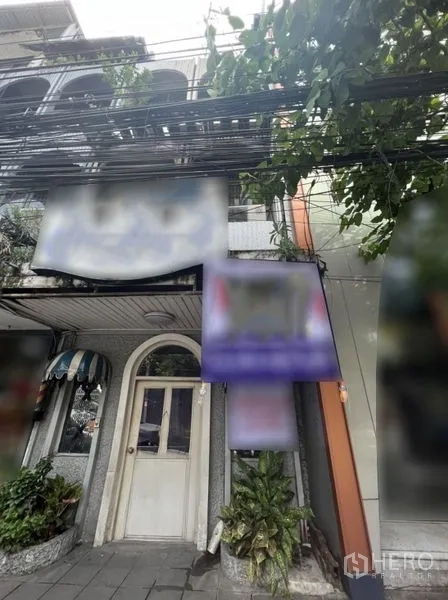 Shophouse for rent in Watthana, Bangkok - Street-facing shophouse facade in Ekkamai, Watthana with arched doorway, signage and greenery.
