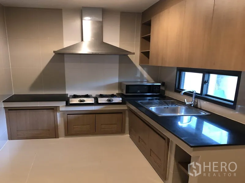 Detached House for rent in Bang Kapi, Bangkok - Built-in kitchen with black countertops, gas hobs, range hood and stainless sink.