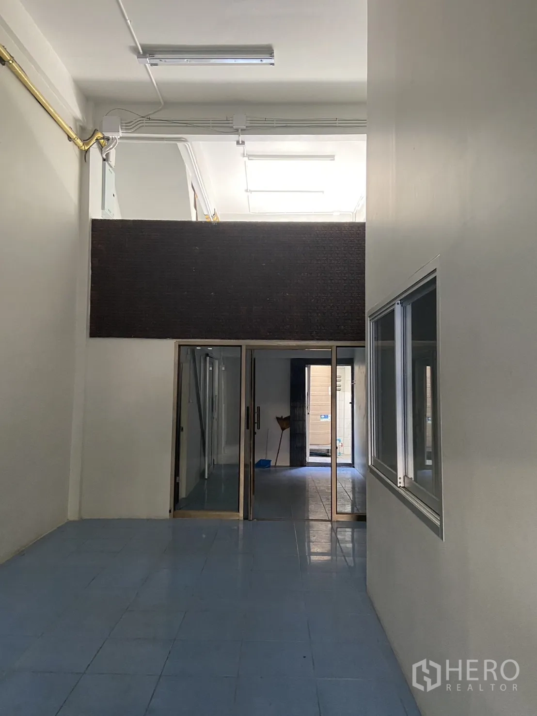 Shophouse for rent in Bang Na, Bangkok - Ground-floor hall with high ceiling, blue tiles and sliding glass partitions leading to the rear area.