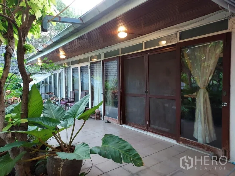Detached House for rent in Mueang Samut Prakan, Samut Prakan - Long veranda with sliding glass doors, warm ceiling lights and greenery.