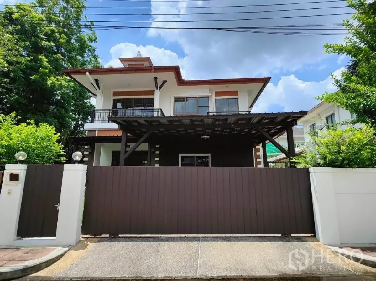 Detached House for rent or sale in Mueang Nonthaburi, Nonthaburi - Modern two-storey detached house with large solid gate and covered carport under a clear sky.