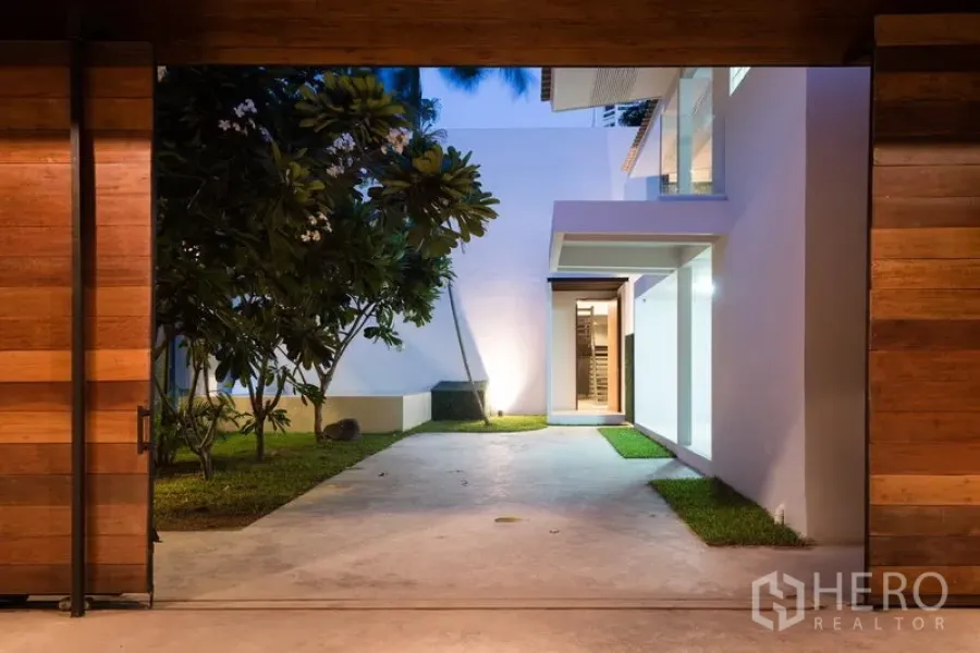 Home Office for rent in Khlong Toei, Bangkok - Sliding wooden gate opening to a modern courtyard with lawn and white facade in Thonglor, Bangkok.