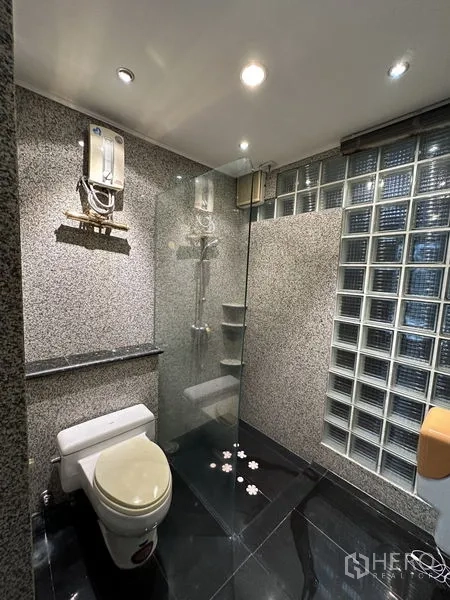Townhouse for rent in Khlong Toei, Bangkok - Compact bathroom with glass shower, granite walls and a glass-block divider.