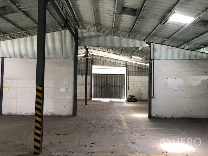Warehouse for rent in Khlong Luang, Pathum Thani - Deep warehouse aisle with high-clearance roof and a large steel gate at the end.