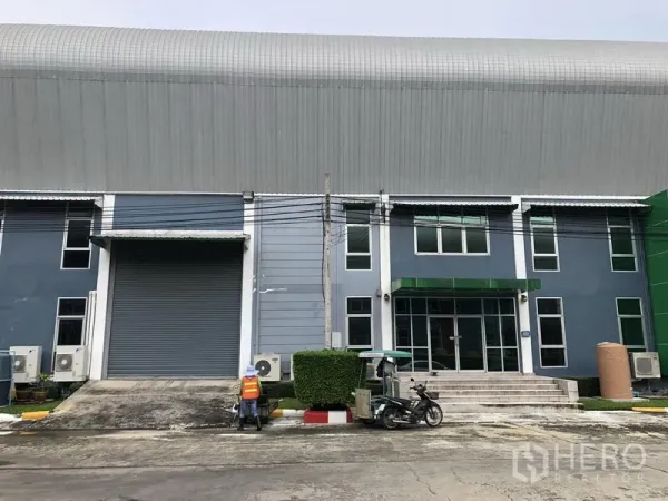 工厂 出租在Samut Prakan - 厂房正立面，设大型装卸卷帘门与玻璃门办公室入口。