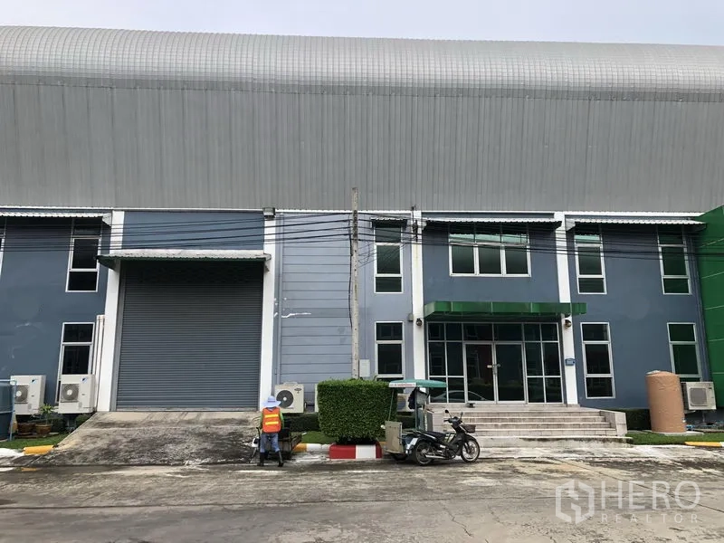 工厂 出租在Samut Prakan - 厂房正立面，设大型装卸卷帘门与玻璃门办公室入口。