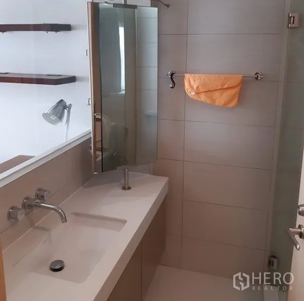 Condominium for rent in Khlong Toei, Bangkok - Contemporary bathroom with long vanity, wall-mounted faucet and tiled shower area.