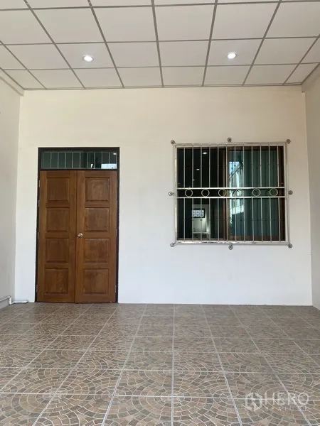 联排别墅 出租在Suan Luang, Bangkok - 带顶前庭，拼花地砖、实木门与带护栏窗户的联排别墅入口。