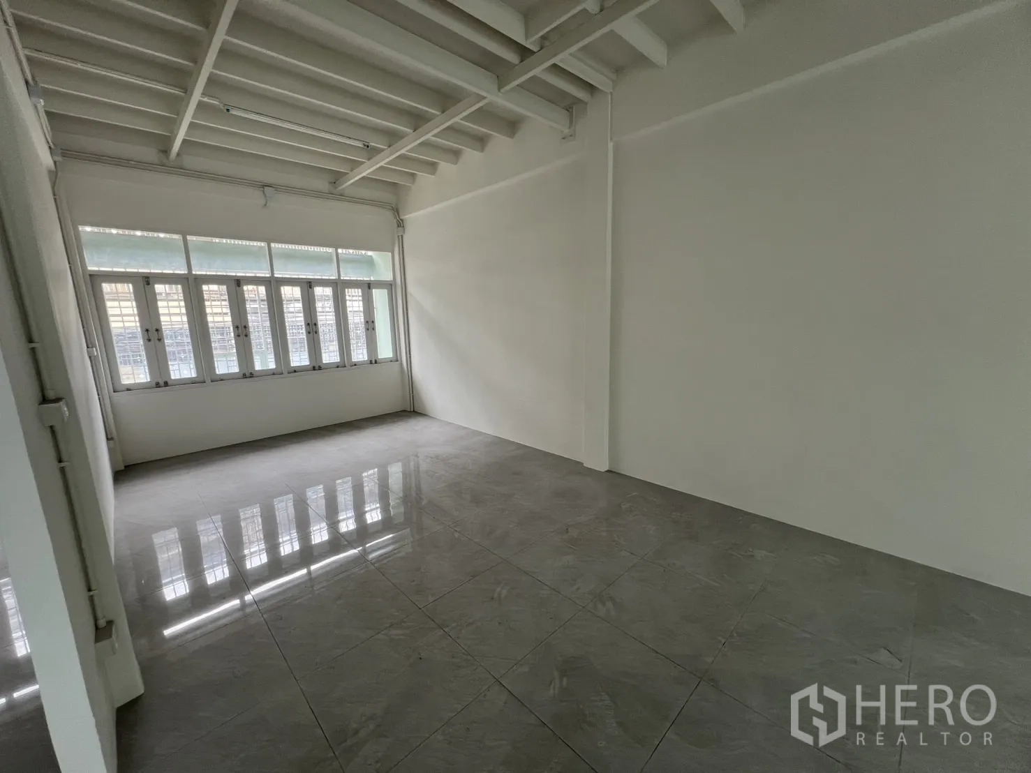 Shophouse for rent in Khlong Toei, Bangkok - Bright tiled office room with full-height windows and beamed ceiling.