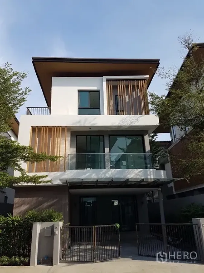 Detached House for rent in Prawet, Bangkok - Modern three-storey detached house exterior with glass balconies, vertical wooden screens and a gated driveway.