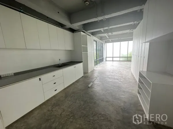 Office Space for rent in Khlong Toei, Bangkok - Open workspace with long run of built-in white cabinetry and pantry sink under an exposed ceiling.