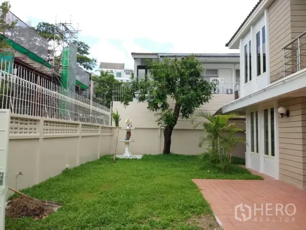 Detached House for rent in Watthana, Bangkok - Private lawn garden with mature tree, boundary wall and paved terrace beside the house.