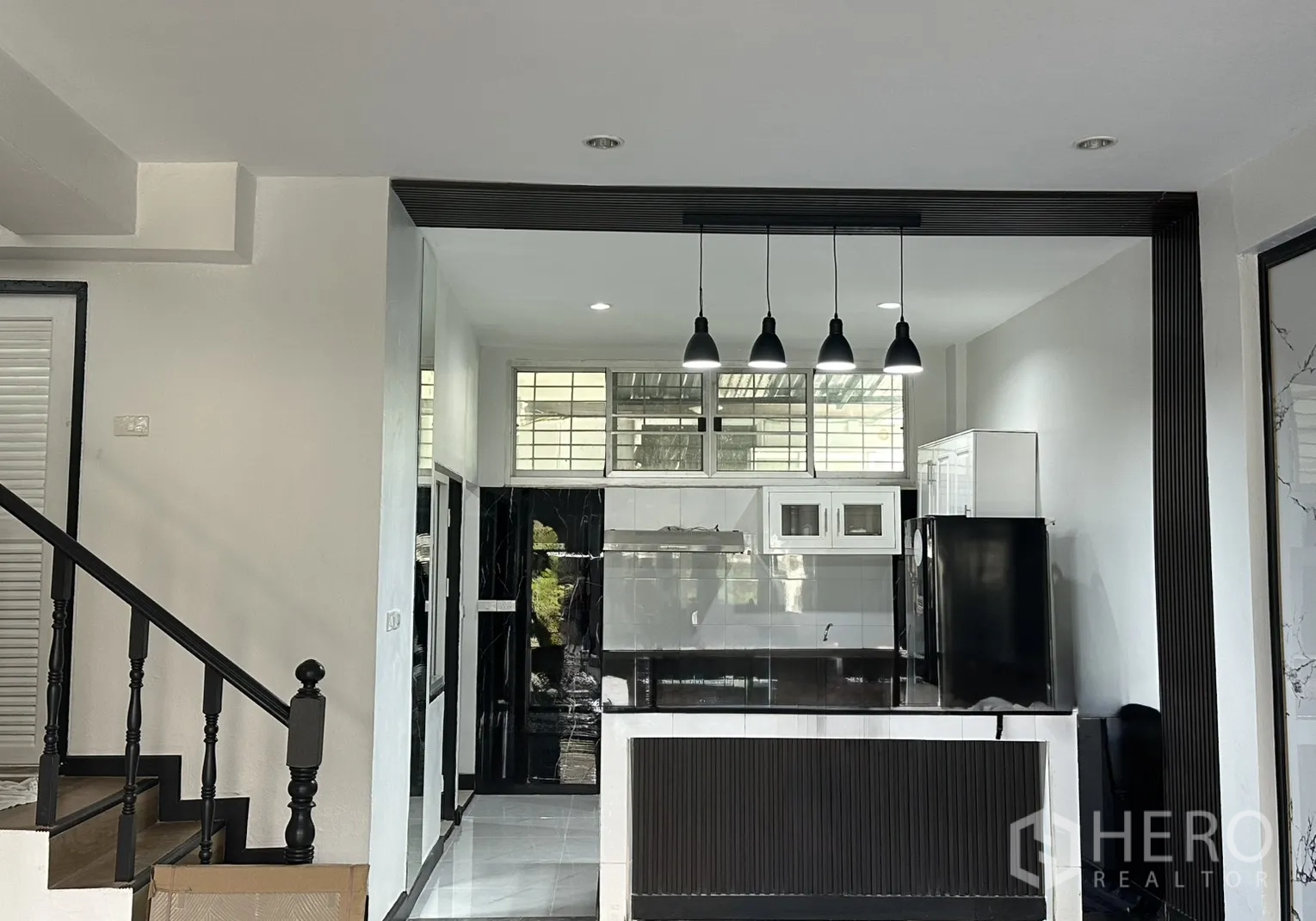Townhouse for rent in Watthana, Bangkok - Black-and-white kitchen with island counter, pendant lights and upper windows.