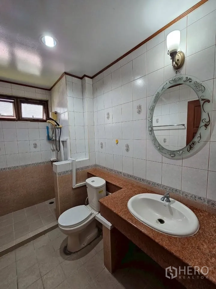Home Office for rent in Wang Thonglang, Bangkok - White tiled bathroom with orange stone counter, toilet and round mirror.